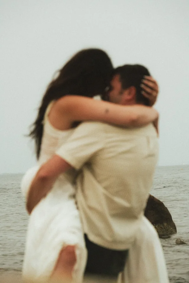 A bride and groom holding each other close, the water behind them.