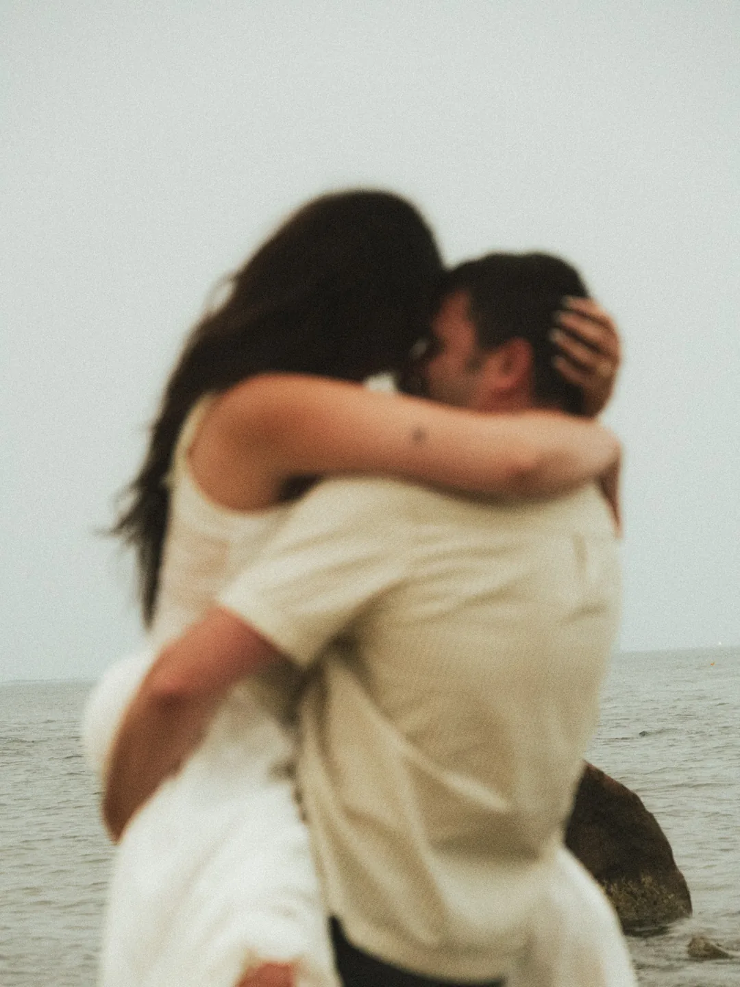 A bride and groom holding each other close, the water behind them.